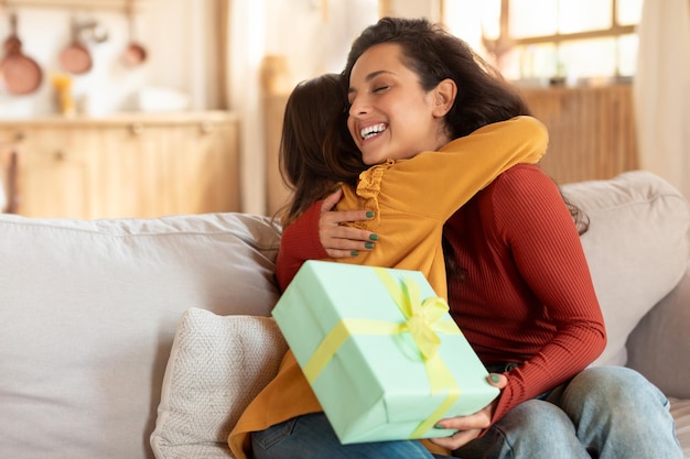 Hija árabe alegre felicitando a mamá dando un regalo en casa