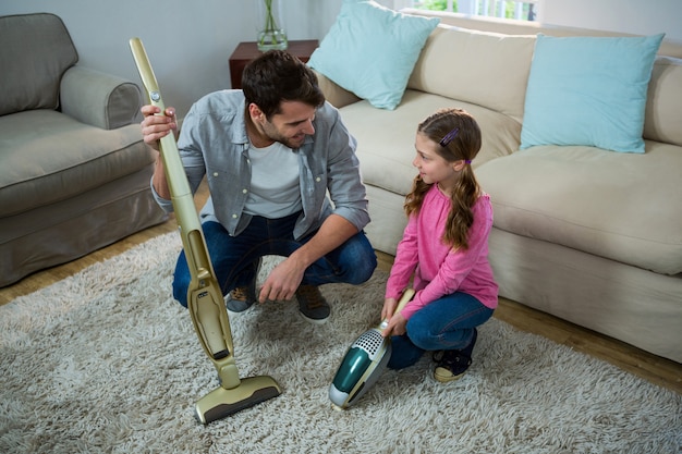 Hija ayudando a su padre a limpiar la alfombra con una aspiradora