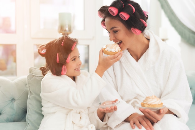 Hija en batas de baño está alimentando a su madre con un pastel