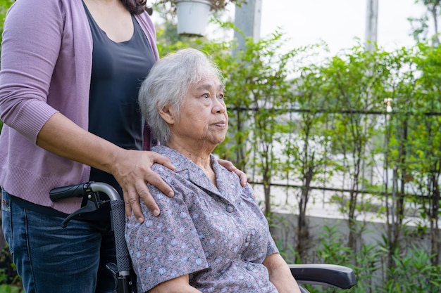 La hija del cuidador ayuda a la anciana asiática mayor o anciana en silla de ruedas eléctrica en el parque.