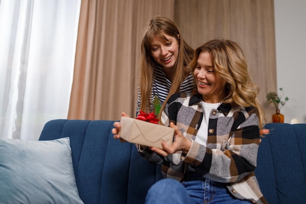La hija le da un regalo a su madre que está sentada en el sofá de la sala de estar