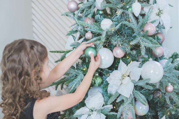 Hija decorando el árbol de navidad colgando adornos antes de las manos de los niños decorati