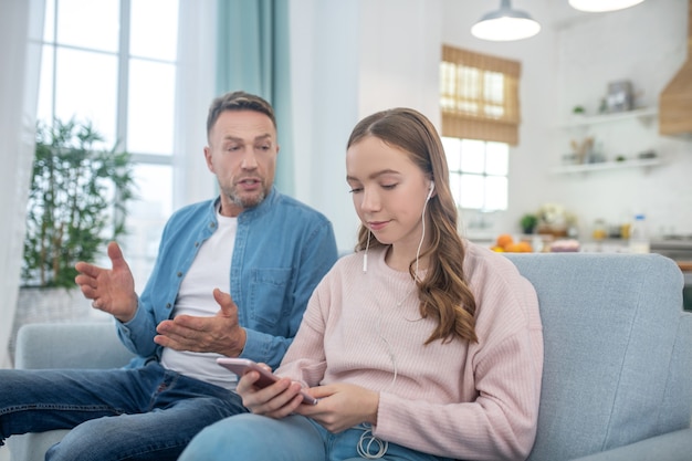 Hija escuchando música con auriculares y con un teléfono inteligente en sus manos