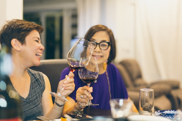 Hija de familia feliz brindando copas de vino tinto con la madre en casa.