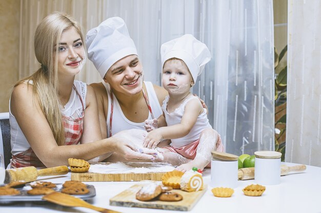 Hija feliz de la familia con papá y mamá en la cocina de casa riendo y preparando la comida juntos