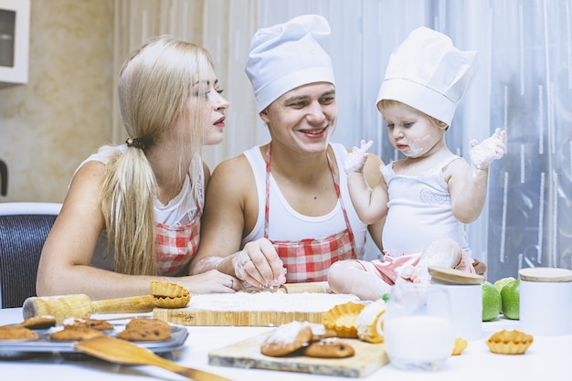 Hija feliz de la familia con papá y mamá en la cocina de casa riendo y preparando la comida juntos