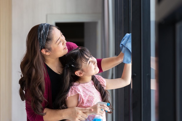 La hija feliz con la mamá madre limpia y lava el vidrio de la ventana juntos como un buen trabajo en equipo para la actividad de limpieza durante el fin de semana en casa