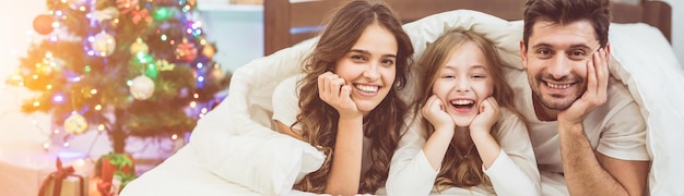 La hija feliz y los padres yacían en la cama cerca del árbol de Navidad.