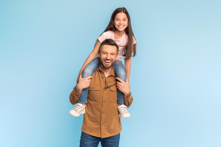 Una hija feliz sentada en los hombros de su padre sobre un fondo azul.