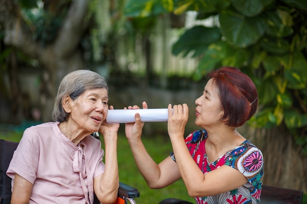 Hija hablando con una anciana con discapacidad auditiva, utilizando un tubo de papel