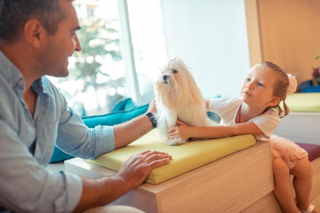 Hija hablando con papá y tocando su perro blanco y esponjoso