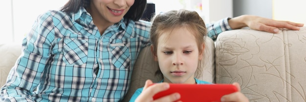 Hija juega videojuegos en línea en un teléfono inteligente y mamá lo ve