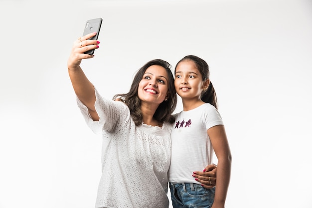 Hija de madre asiática india tomando selfie foto con smartphone, aislado sobre fondo blanco.