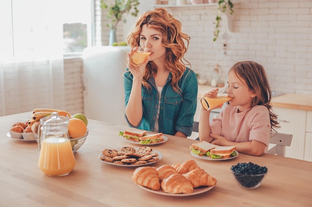 Hija y madre bebiendo jugo de naranja para desayunar en la cocina doméstica