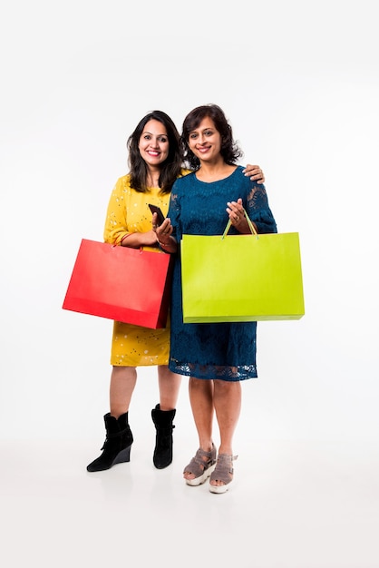 Hija de madre india hermanas compras con bolsas de colores, que se encuentran aisladas sobre fondo blanco.