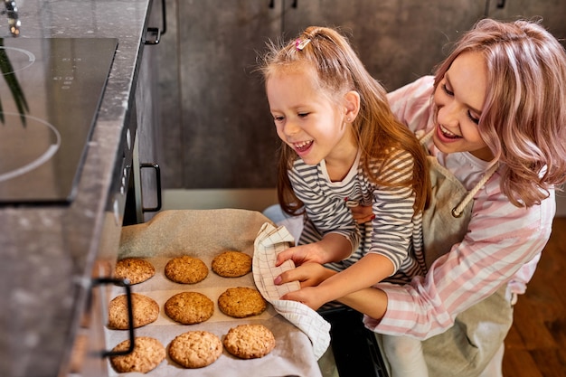 Hija y madre sacando la bandeja de galletas horneadas del horno en la cocina