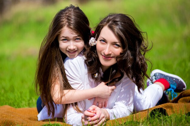 Hija con la madre sentada en el césped en la primavera y comunicarse