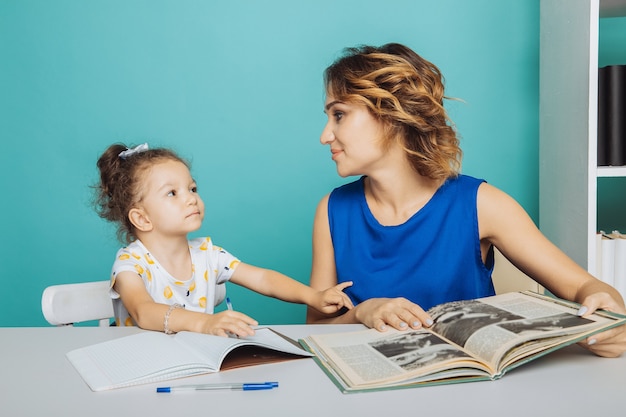 Hija con madre sentados juntos a la mesa y haciendo los deberes.