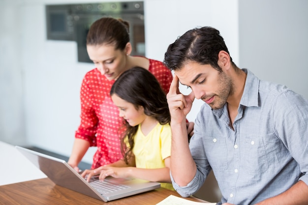 Hija y madre trabajando en la computadora portátil con tenso padre sentado en el escritorio