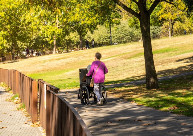 Hija mayor ayudando a su anciana madre a caminar en su silla de ruedas por un parque