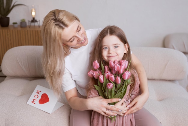 La hija del niño felicita a su madre y le regala flores tulipanes y una tarjeta Mamá