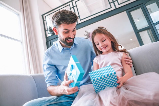 Hija y padre abriendo caja de regalo mientras se sientan en el sofá en casa