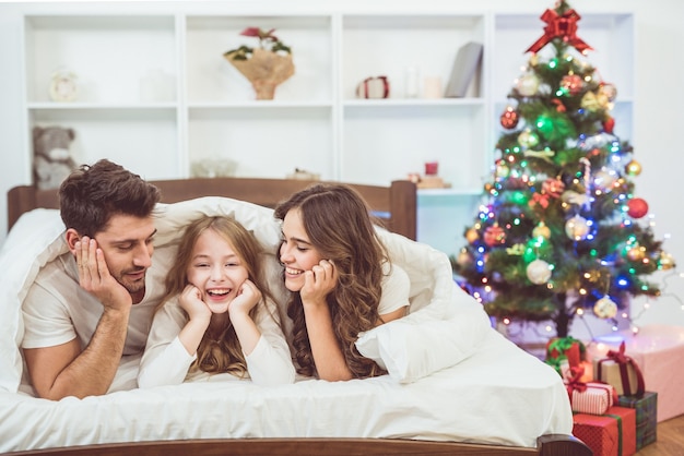 La hija y los padres yacían en la cama cerca del árbol de navidad.