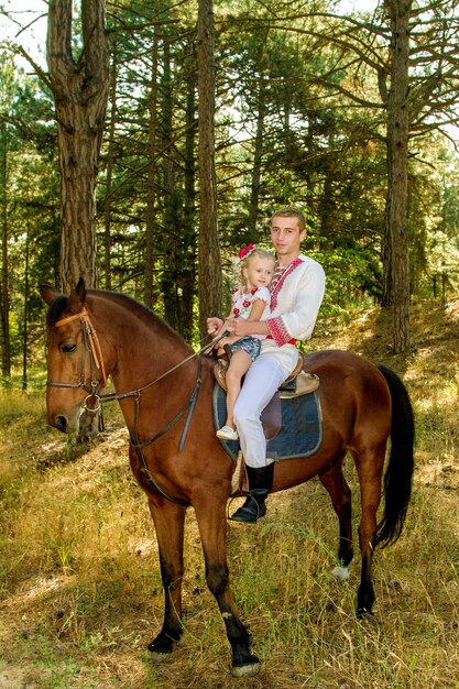 Hija de papá joven rueda sobre el caballo en el bosque