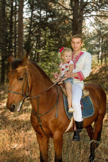 Hija de papá joven rueda sobre el caballo en el bosque