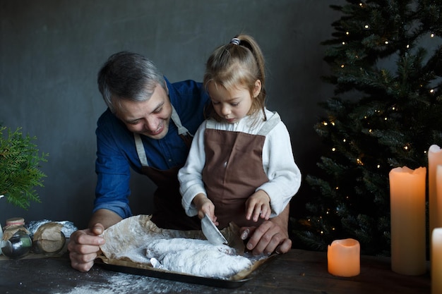 Una hija pequeña y su padre están preparando un stollen de Navidad en la cocina con su azúcar en polvo