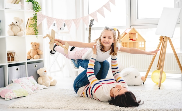 Hija riendo volando sobre las piernas de la madre