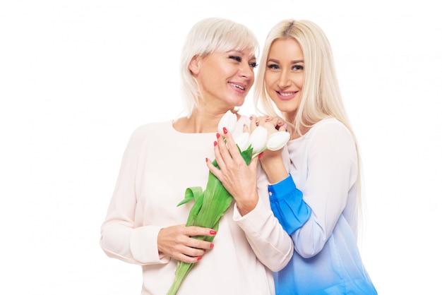 Hija rubia adolescente y madre madura sobre fondo azul abrazando