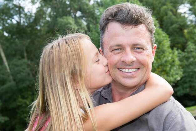 Hija rubia alegre intenta besar a su padre sonriente