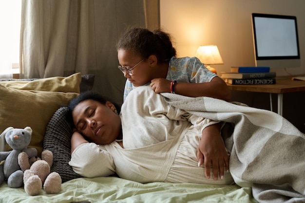 La hija sentada en la cama junto a su madre embarazada mientras ella duerme