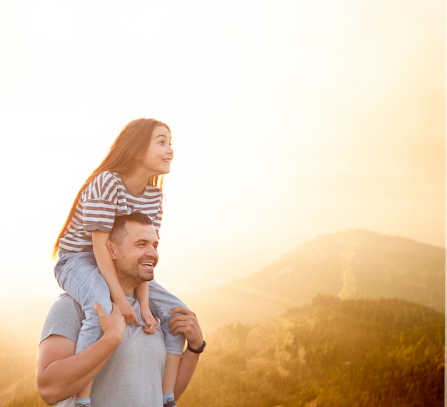 la hija se sienta sobre los hombros de papá al aire libre contra el telón de fondo de las montañas al sol