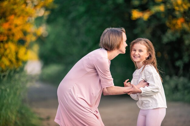 Hija con su madre, una familia feliz pasear por el parque en una tarde de verano, mirarse, reír alegremente, la suave luz del atardecer