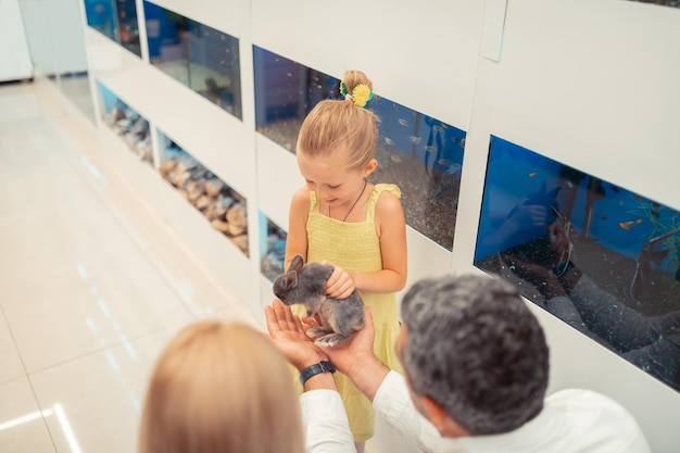 Foto hija tocando conejo mientras viene a la tienda de mascotas con sus padres