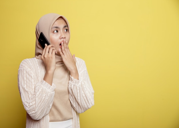 Hijab de mulher com expressão chocada de telefone chamando isolado em fundo amarelo