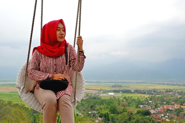 Hijab-Frau genießt die Aussicht auf der Schaukel von der Spitze des Hügels in Eling Bening