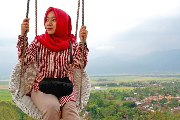 Hijab-Frau genießt die Aussicht auf der Schaukel von der Spitze des Hügels in Eling Bening