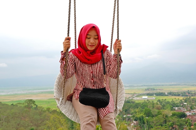 Hijab-Frau genießt die Aussicht auf der Schaukel von der Spitze des Hügels in Eling Bening