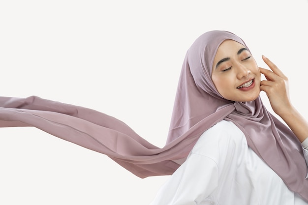 Hijab-Mädchen, das es genießt, einen lila Schleier zu tragen, der mit einer Handbewegung auf der Wange im Wind weht