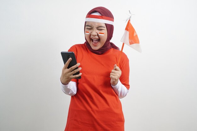 Foto hijab de mujer feliz con bandera roja y blanca con teléfono inteligente