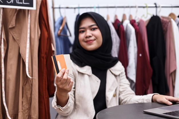 Hijab mujer sosteniendo tarjetas de crédito en la tienda de ropa Servicio de pago con tarjeta de crédito