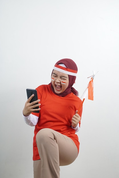 Hijab de mujer sostiene bandera roja y blanca con teléfono celular de juego