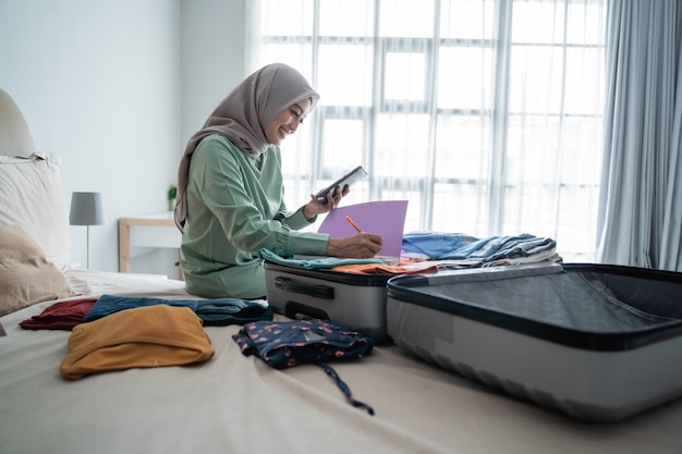 Hijab mulher sentada na cama enquanto olha para a lista de itens