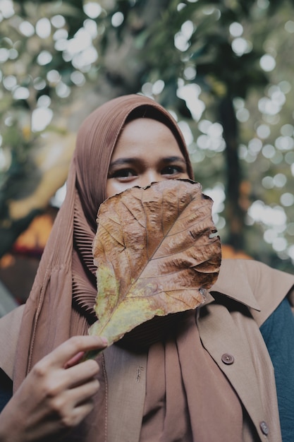 Foto hijab segurando uma grande folha cobrindo o rosto