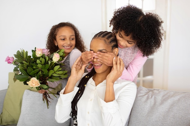 Hijas africanas cerrando los ojos de las madres sorprendiéndola con un ramo en el interior