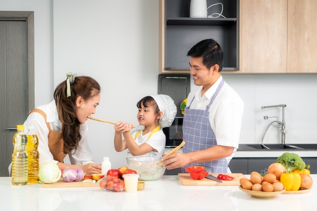 Las hijas asiáticas alimentan la ensalada a su madre y su padre están esperando cuando una familia cocina