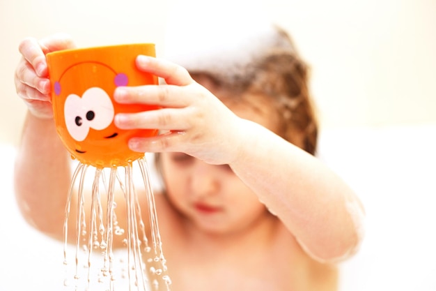 Hijita con cabello rubio jugando con espuma en una tina de baño niña toma un baño